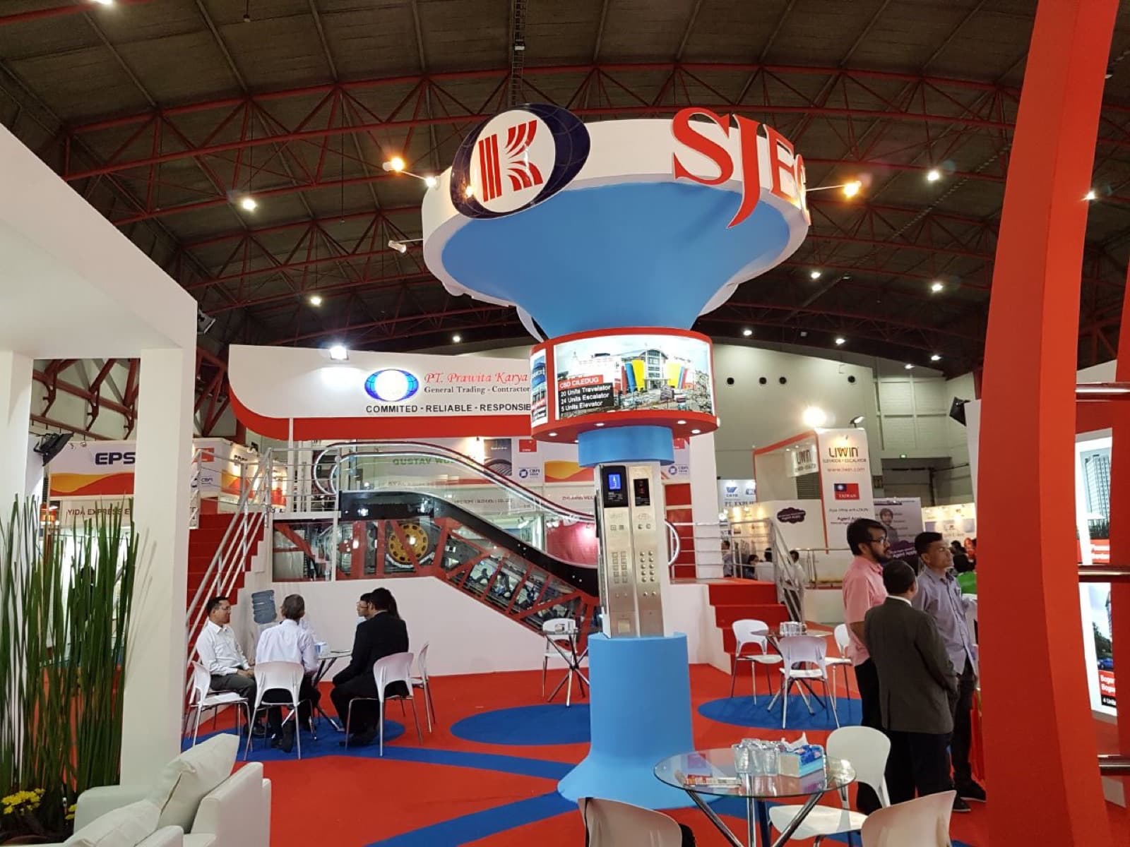 The Prawita Karya and SJEC stand at the Indonesia Lift & Escalator Expo 2016, a double-height structure with a suspended SJEC sign above a working escalator and lift car
