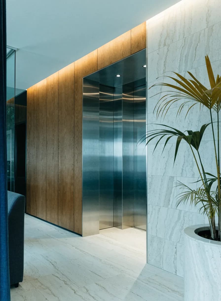 Residential apartment lobby with two stainless steel elevator doors and timber panelling