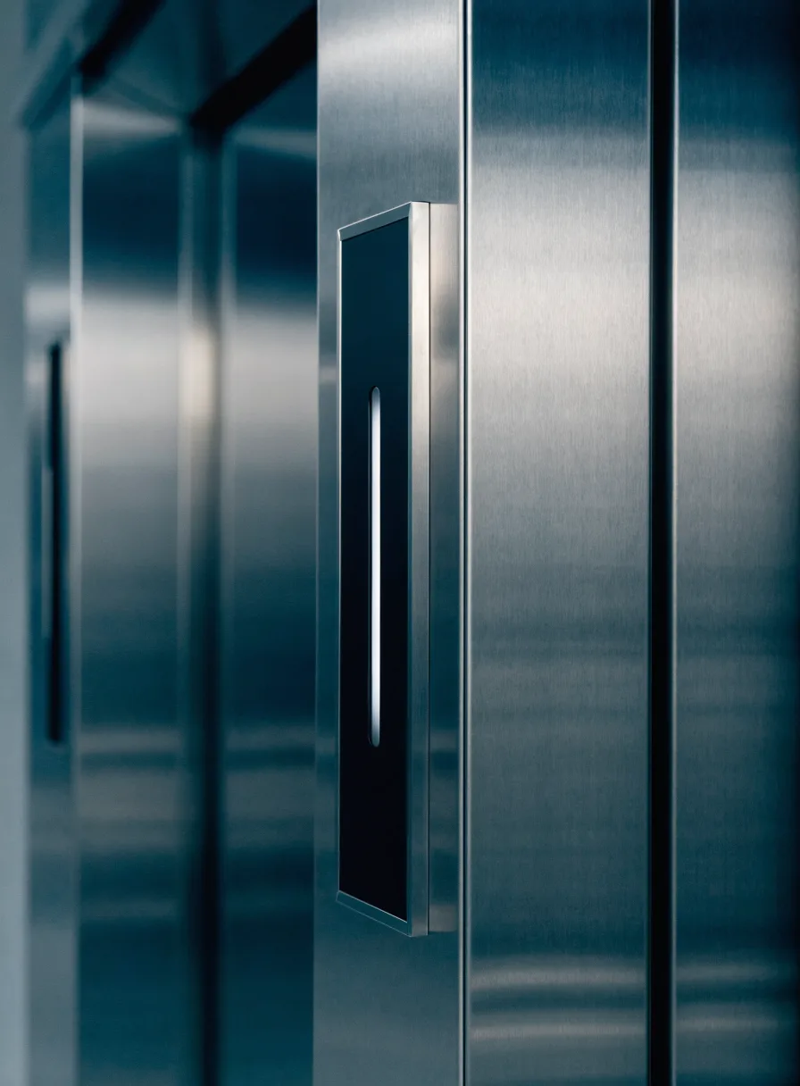 Detail of a brushed stainless steel elevator landing door with a slim call panel and illuminated indicator strip