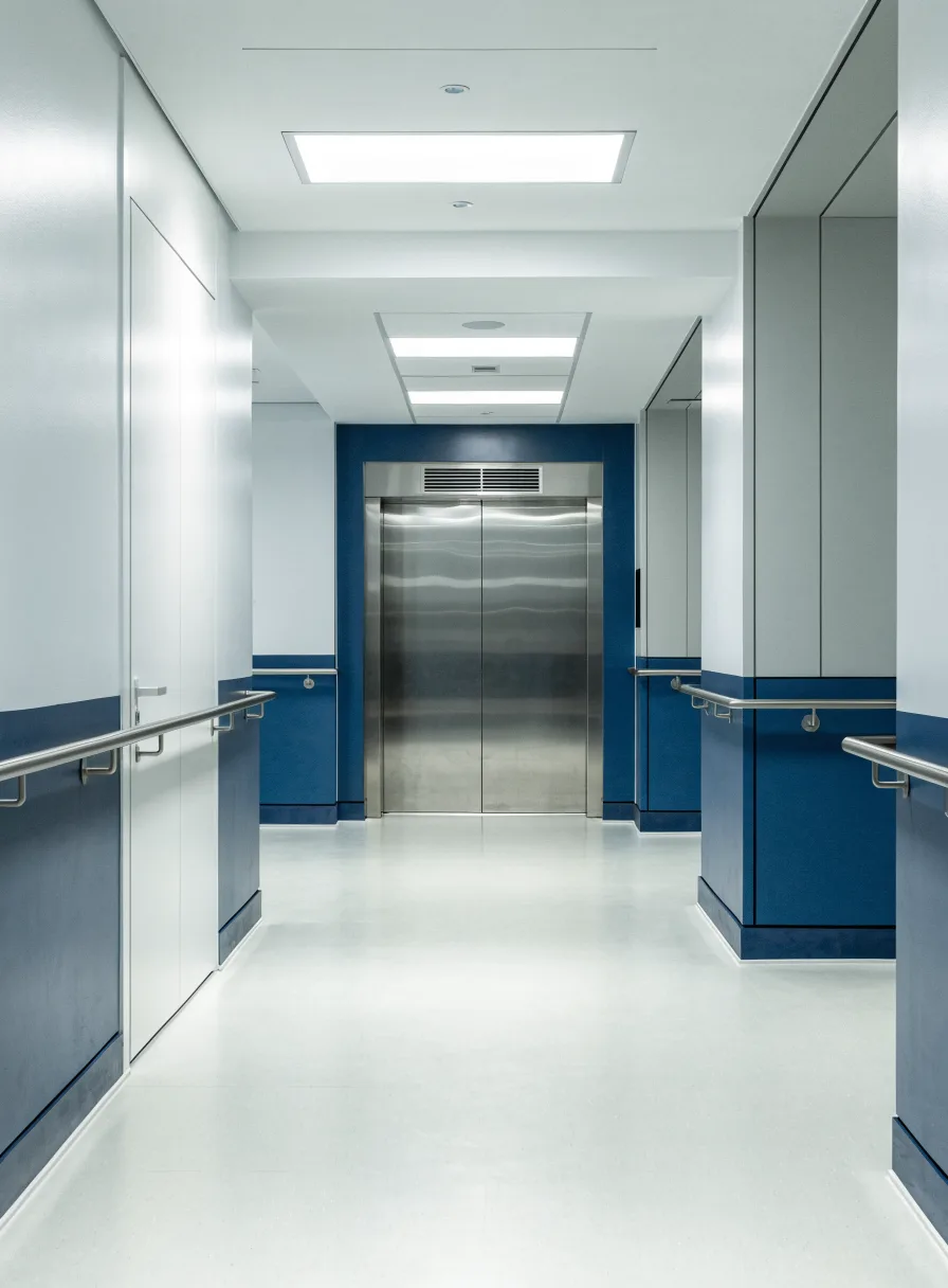 Hospital corridor leading to a wide bed elevator with stainless steel doors