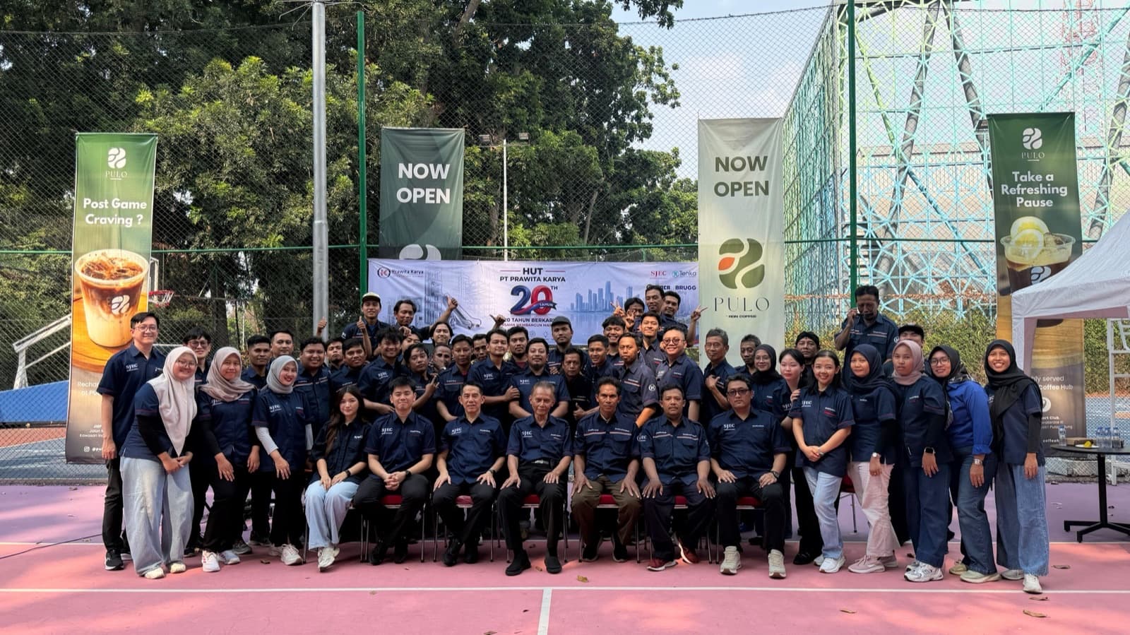 The Prawita Karya and SJEC team photographed together beneath the anniversary banner at Kawasan Industri Pulogadung