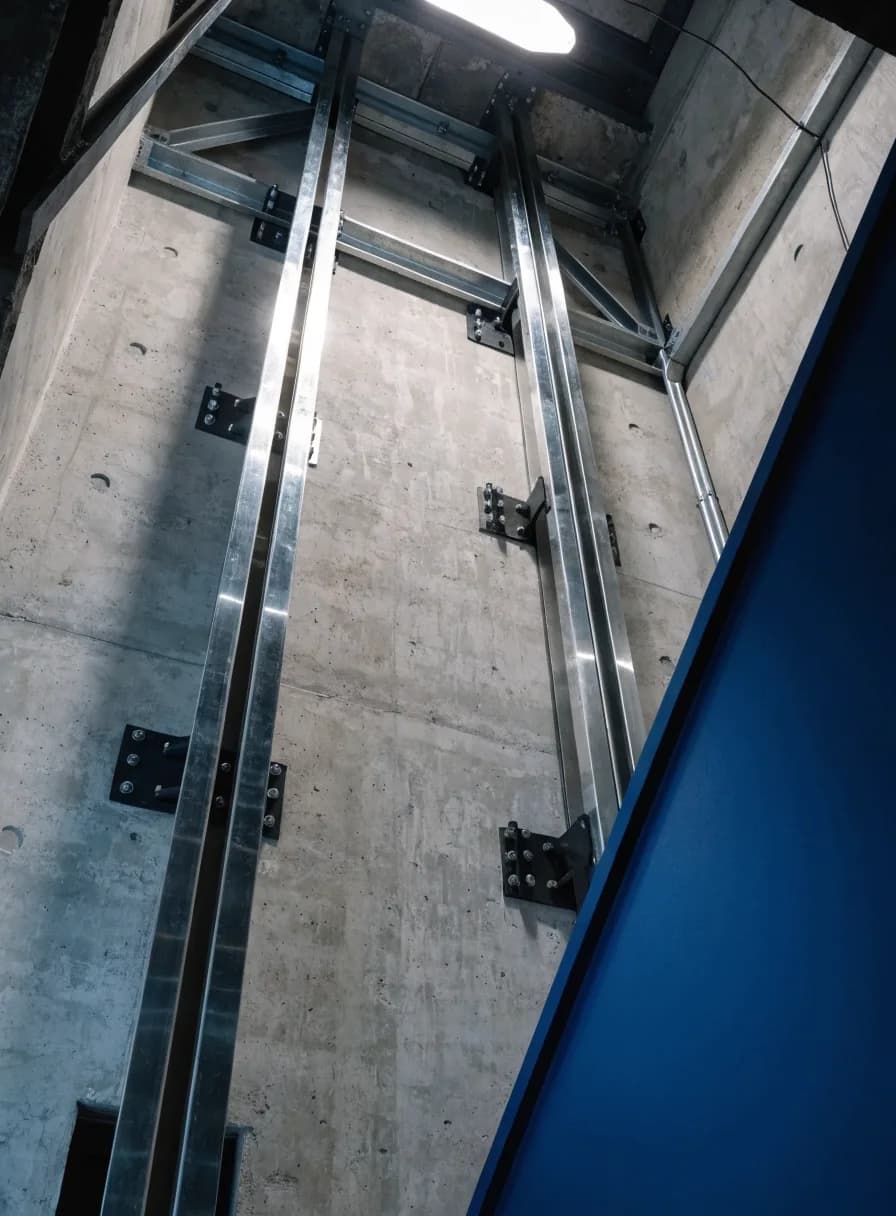 Vertical steel guide rails bolted to a concrete elevator shaft wall during installation