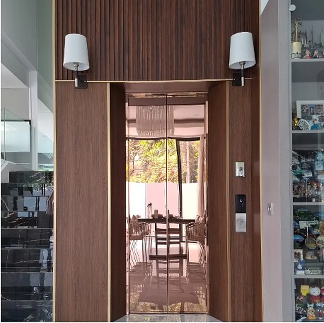 Home lift in a timber-panelled wall between wall lights at a private house in Kemang, Jakarta