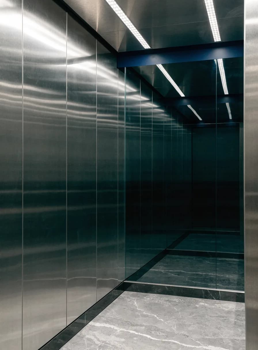 Interior of a modern passenger elevator cabin with brushed stainless steel walls and a glass rear wall
