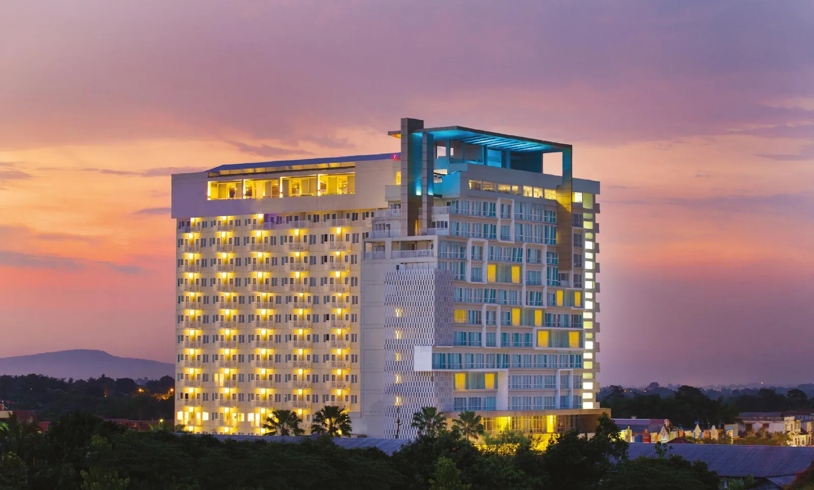 Swiss-Belcourt Hotel at Bogor Icon lit at dusk, with the mountains behind