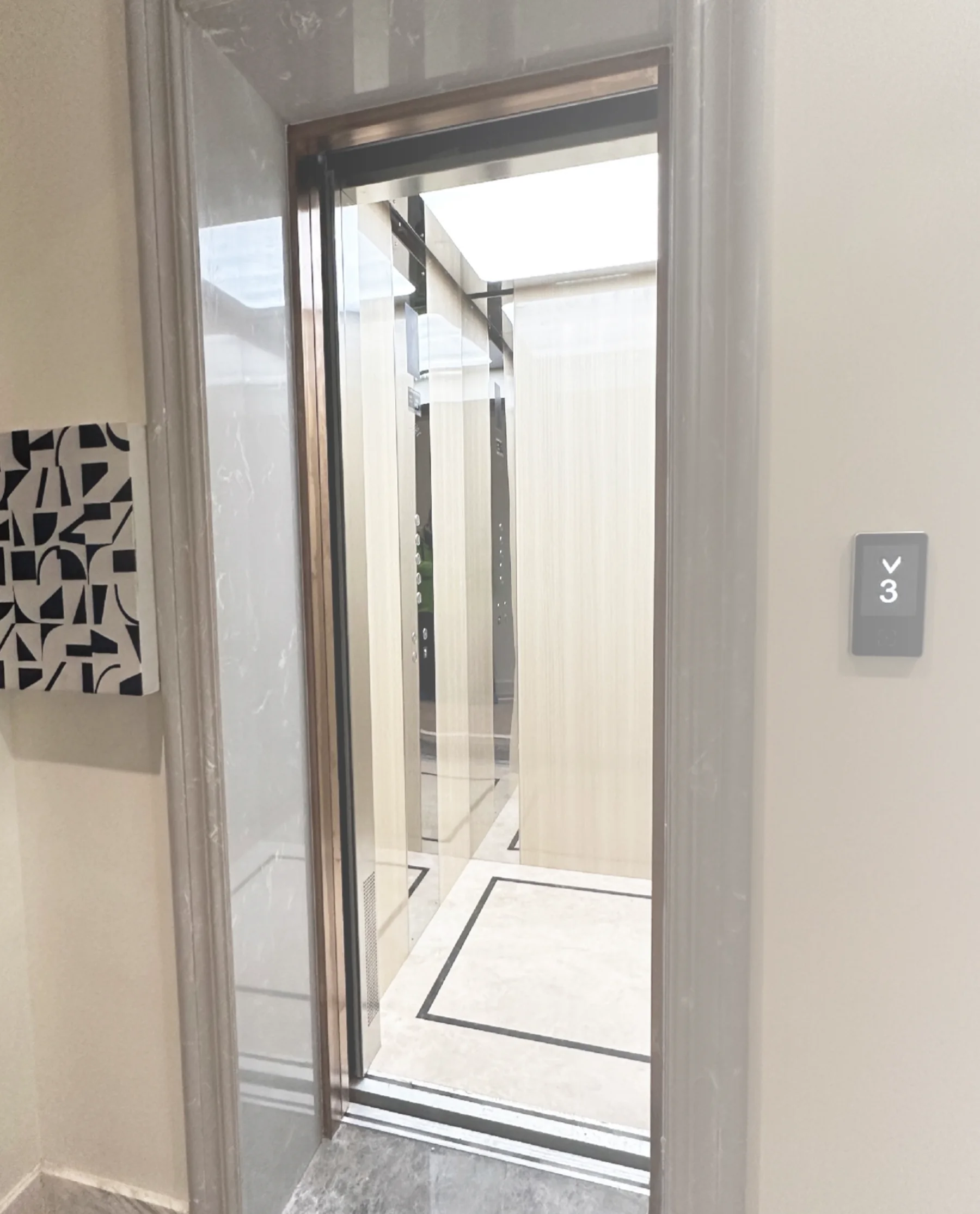 Tenkai V300 home lift at a landing, its glazed door open onto a hairline stainless car, with the landing call panel alongside