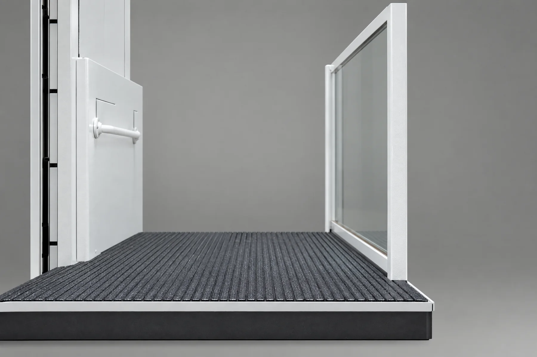 Close-up of a wheelchair platform lift deck: the ribbed anti-slip platform, its white steel edge and the foot of the glass side guard